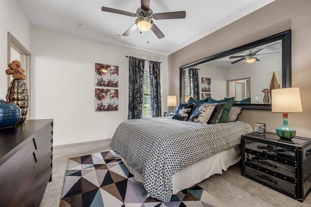 a bedroom with a large bed, dresser, nightstand, mirror, and ceiling fan at Marquis on Lakeline in Cedar Park, TX.