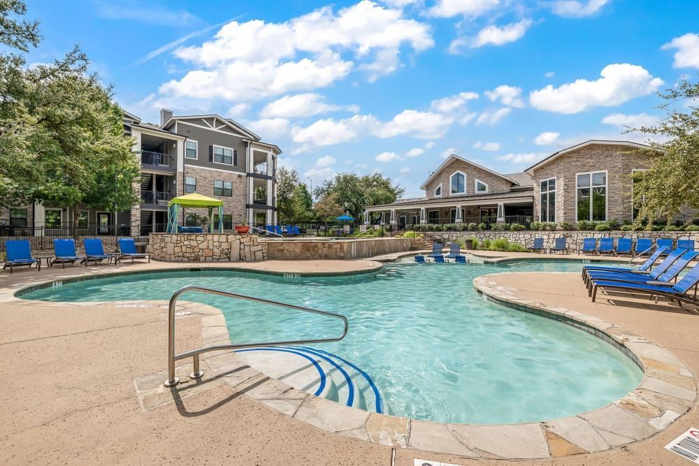 a large swimming pool surrounded by chairs and umbrellas in front of a building at Marquis on Lakeline in Cedar Park, TX.