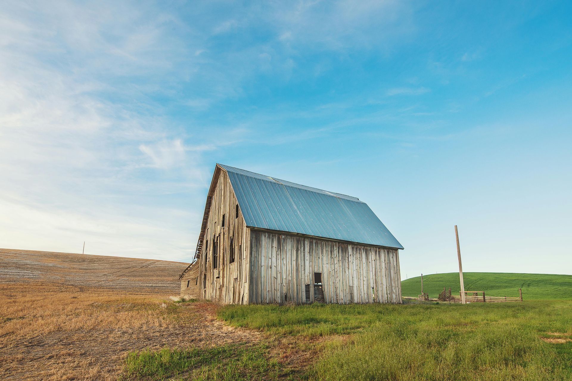 An old barn with a metal roof is sitting in the middle of a grassy field.