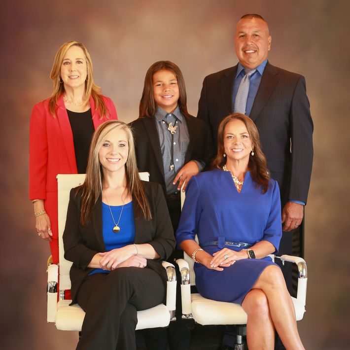 Group photo: five formally dressed people, including a child, against a blurred backdrop.