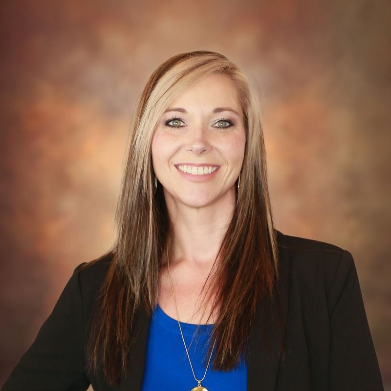 Woman with blonde and brown hair, wearing a black blazer, blue shirt, and smiling.