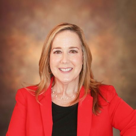 Woman with blonde hair in red blazer smiles at camera.