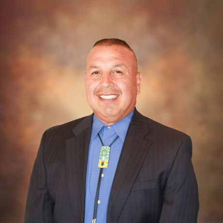Smiling man in a suit and bolo tie, against a blurred backdrop.