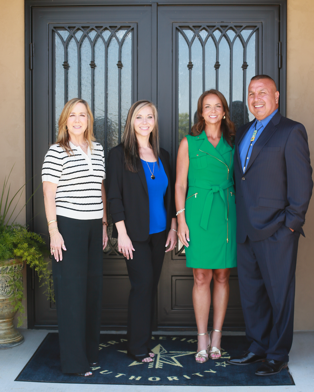 Four professionals pose in front of a dark door, wearing business attire.