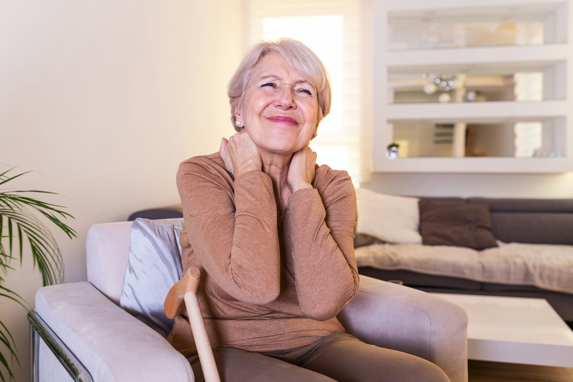 Woman in orange shirt with arms raised, holding a hat, in a field, mountains in background.