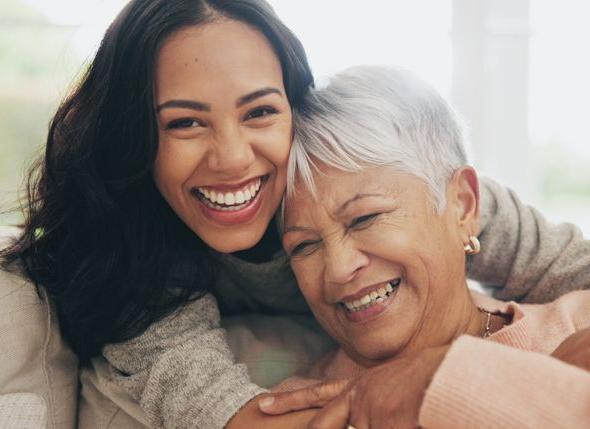 Young woman hugs older woman, both smiling broadly.