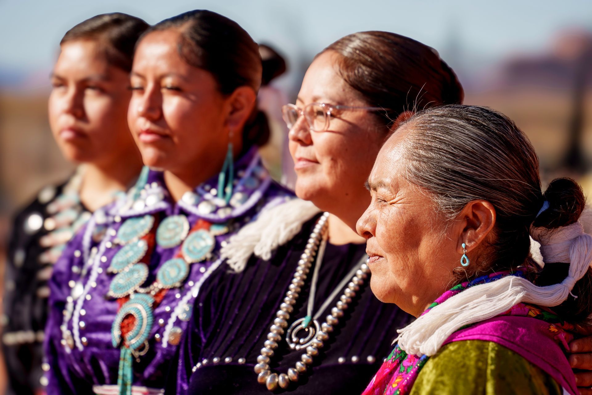 Four Indigenous women in traditional attire, wearing silver and turquoise jewelry, looking right.