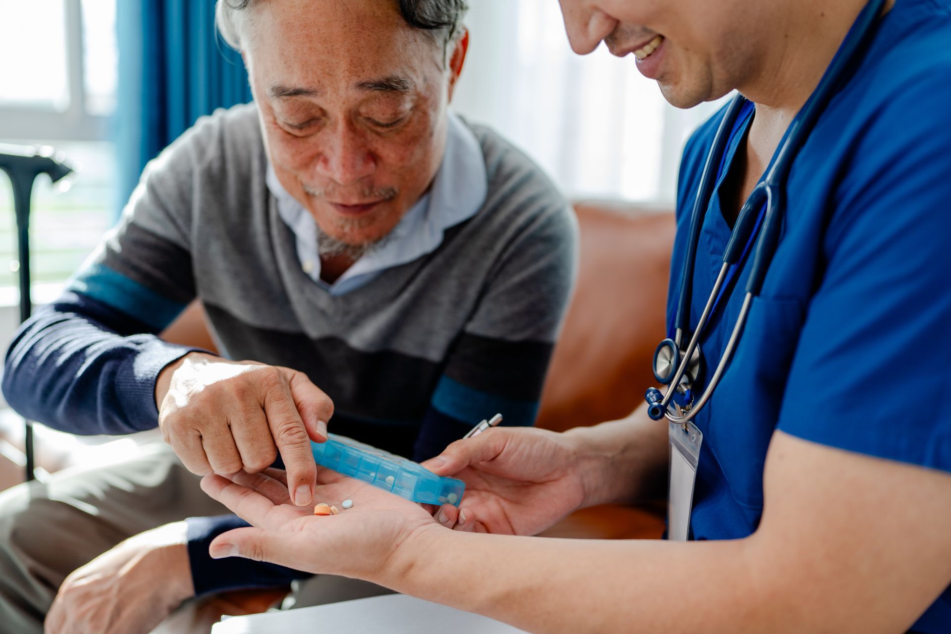 Caregiver helping senior man take pills from pill organizer.