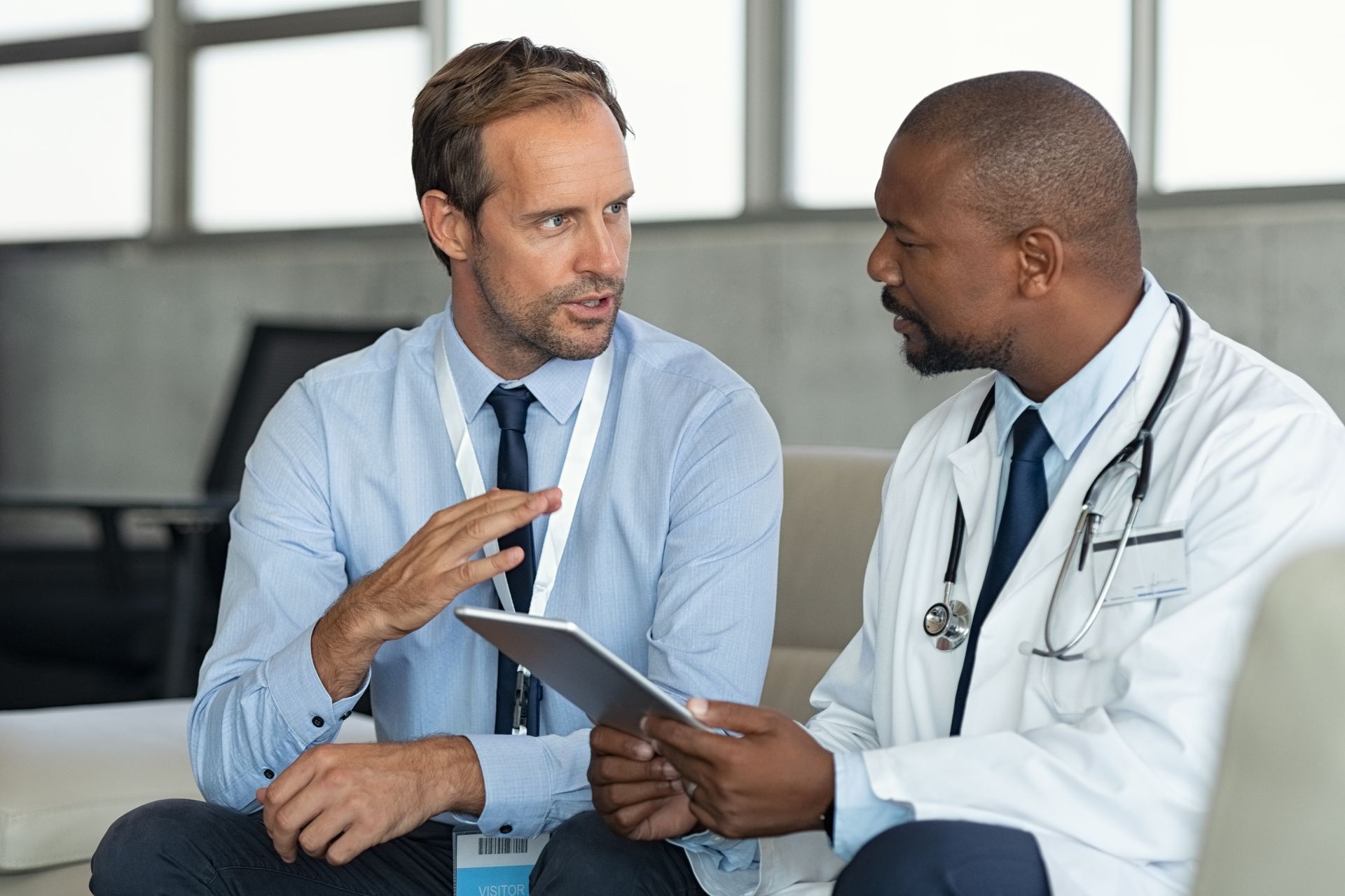 Man in business attire and doctor discussing a tablet in an office setting.