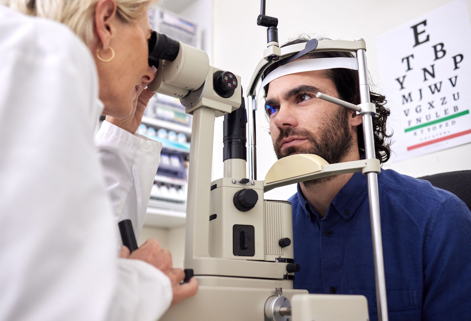 Optometrist examining a man's eye with a slit lamp. Eye chart in the background.