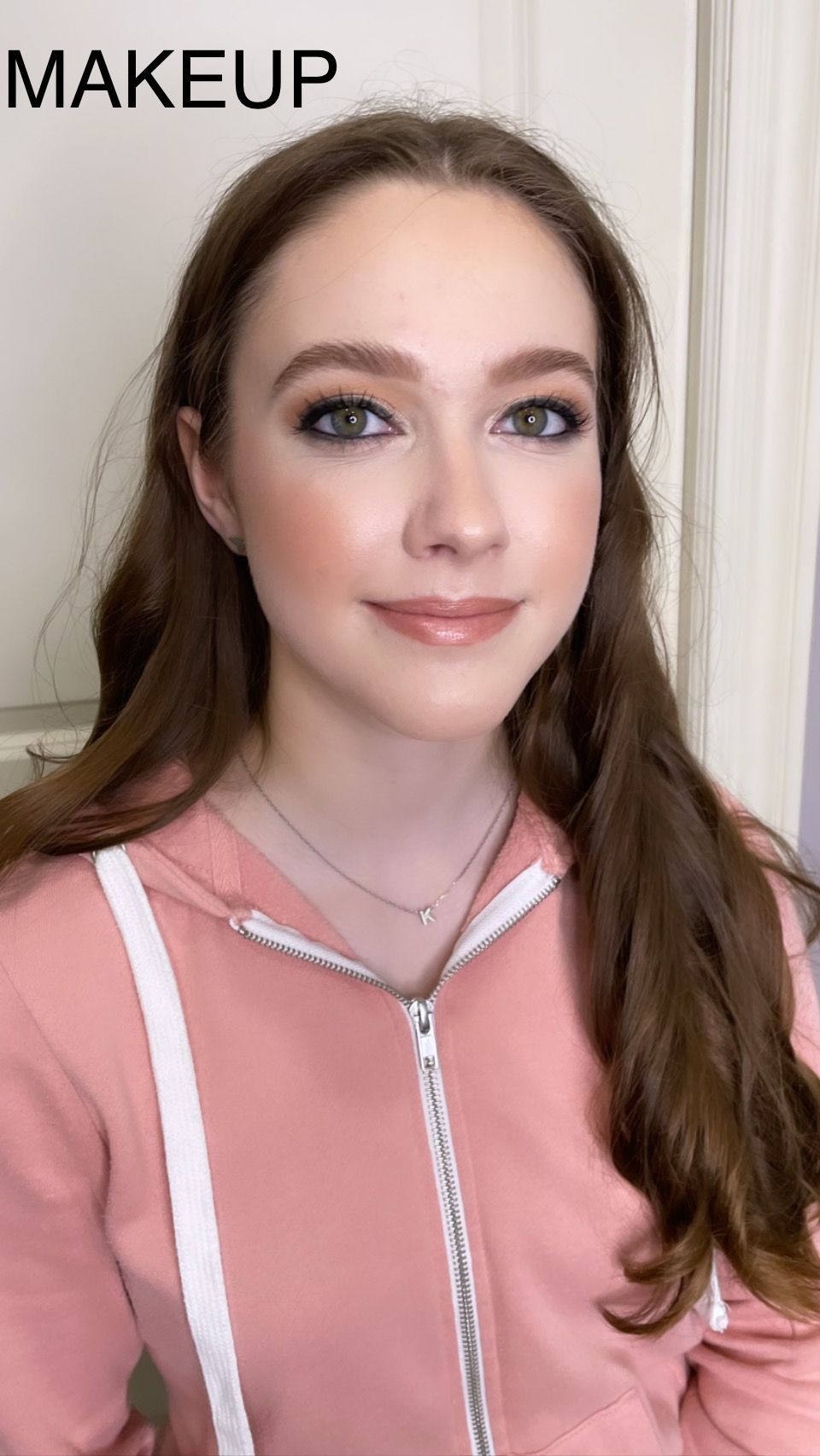 A woman is wearing a pink hoodie and a necklace.