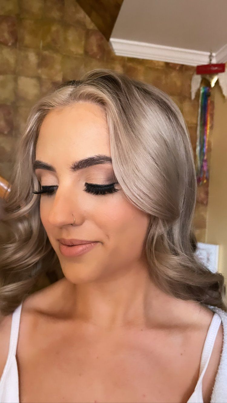 A woman with blonde hair and long eyelashes is getting her makeup done.