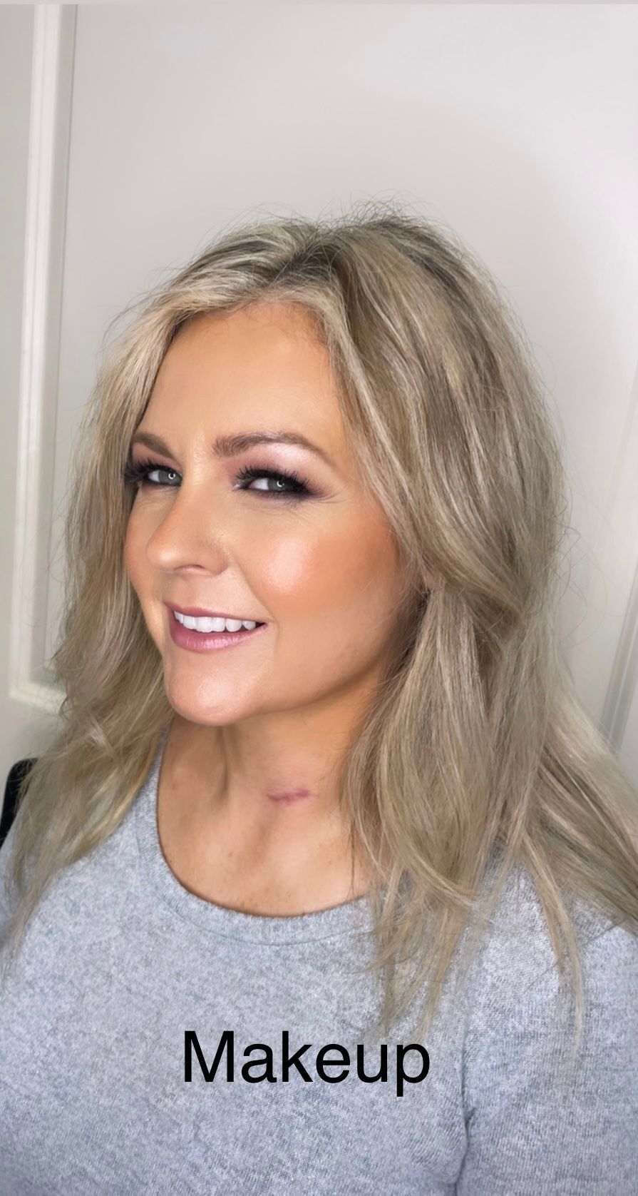 A woman with blonde hair is wearing a grey shirt and smiling.