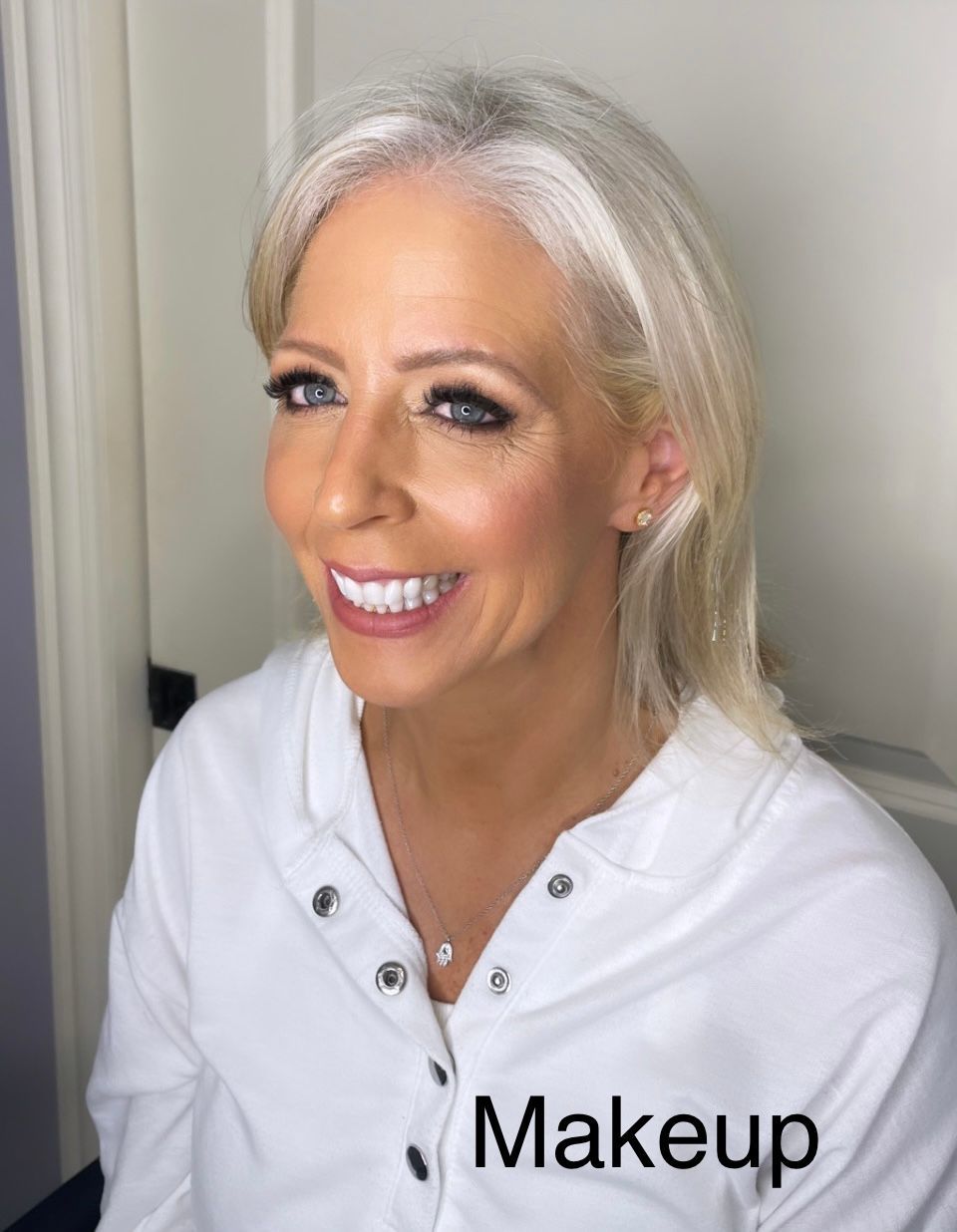 A woman is smiling and wearing a white shirt with the word makeup on it.