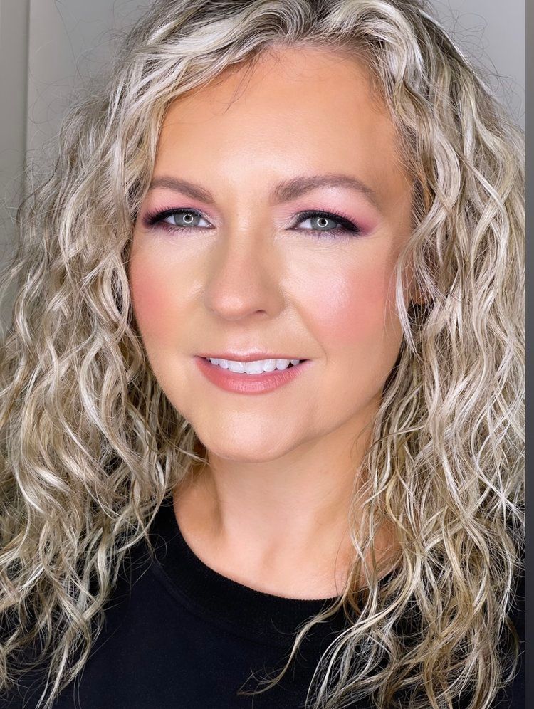 A woman with blonde curly hair is wearing a black shirt and smiling.
