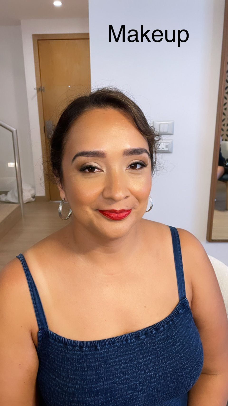 A woman is smiling while getting her makeup done in front of a mirror.