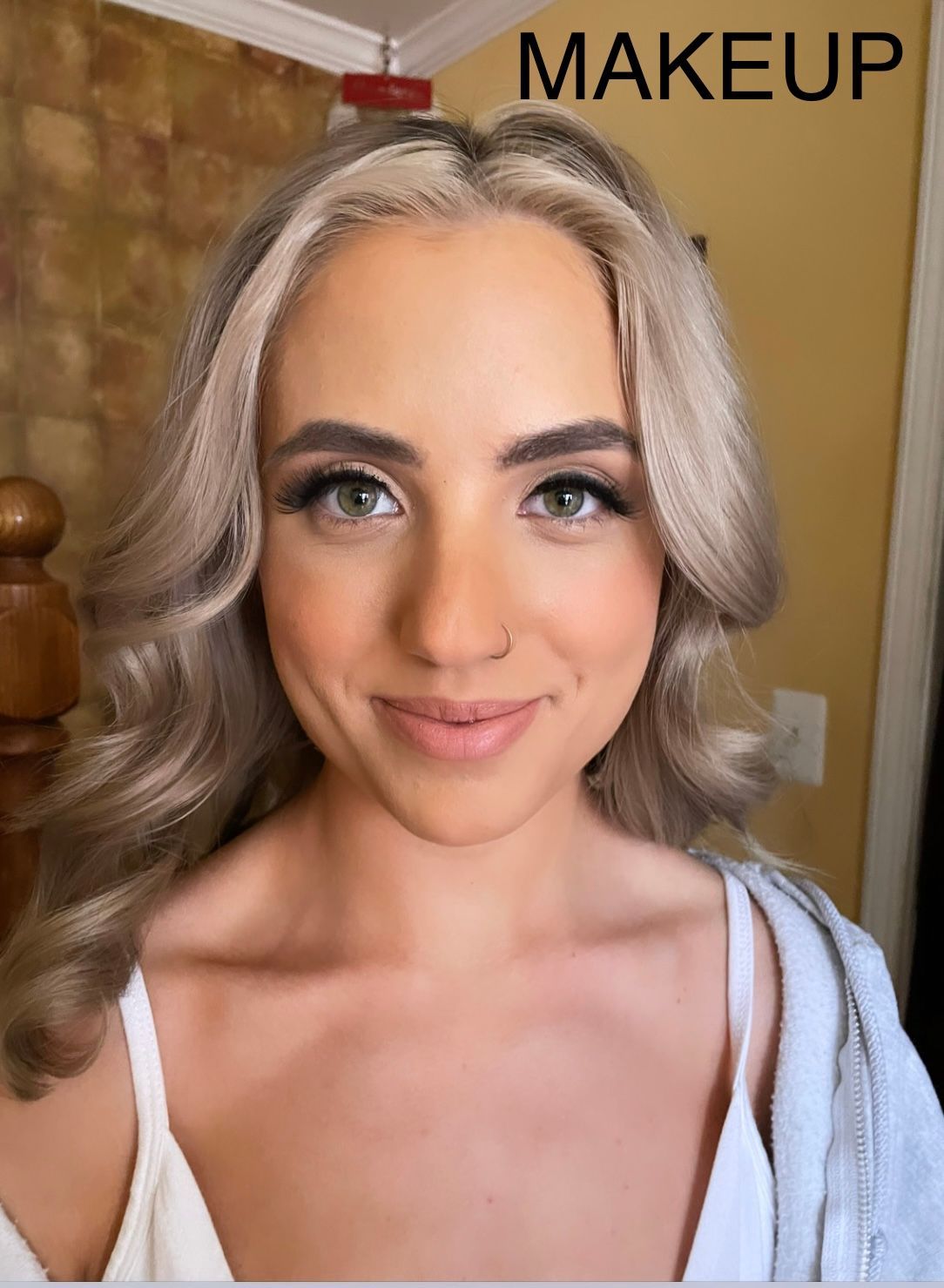 A woman with blonde hair is smiling and wearing makeup.