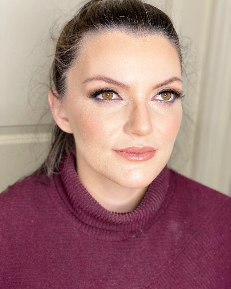 A woman wearing a purple sweater and a ponytail is looking at the camera.