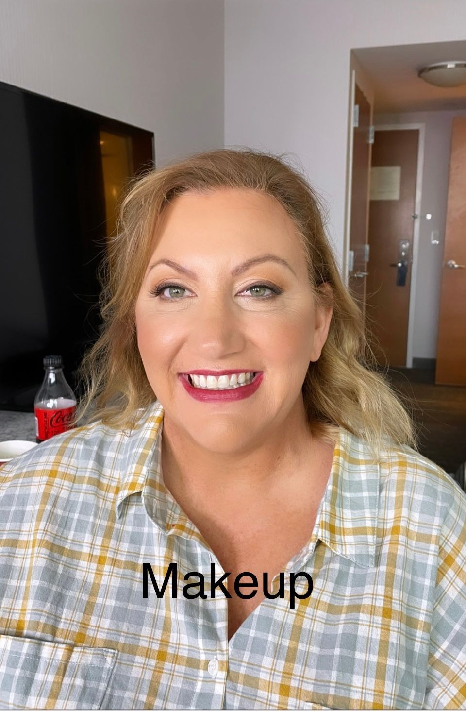 A woman in a plaid shirt is smiling in a hotel room.