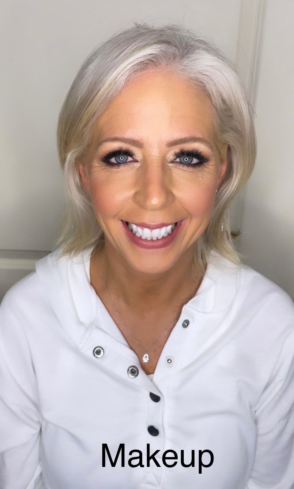 A woman in a white shirt is smiling and wearing makeup.