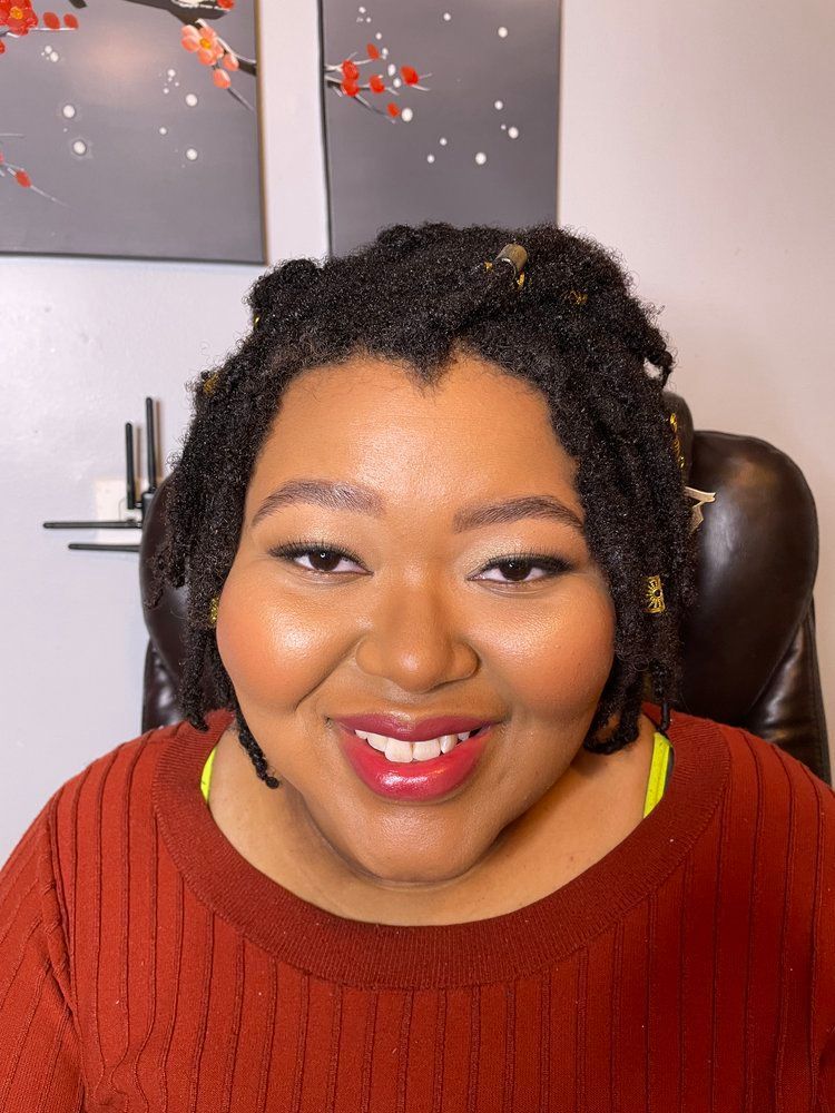 A woman with dreadlocks is smiling and wearing a red sweater.