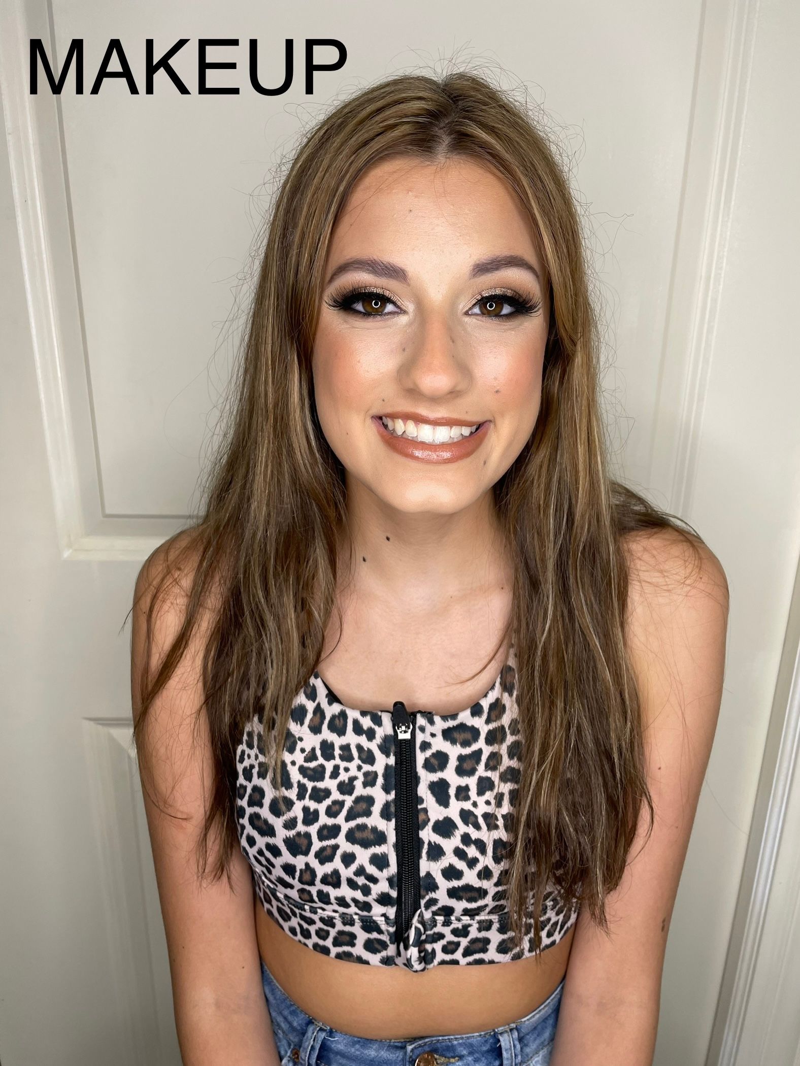 A young woman wearing a leopard print crop top and jeans is smiling.