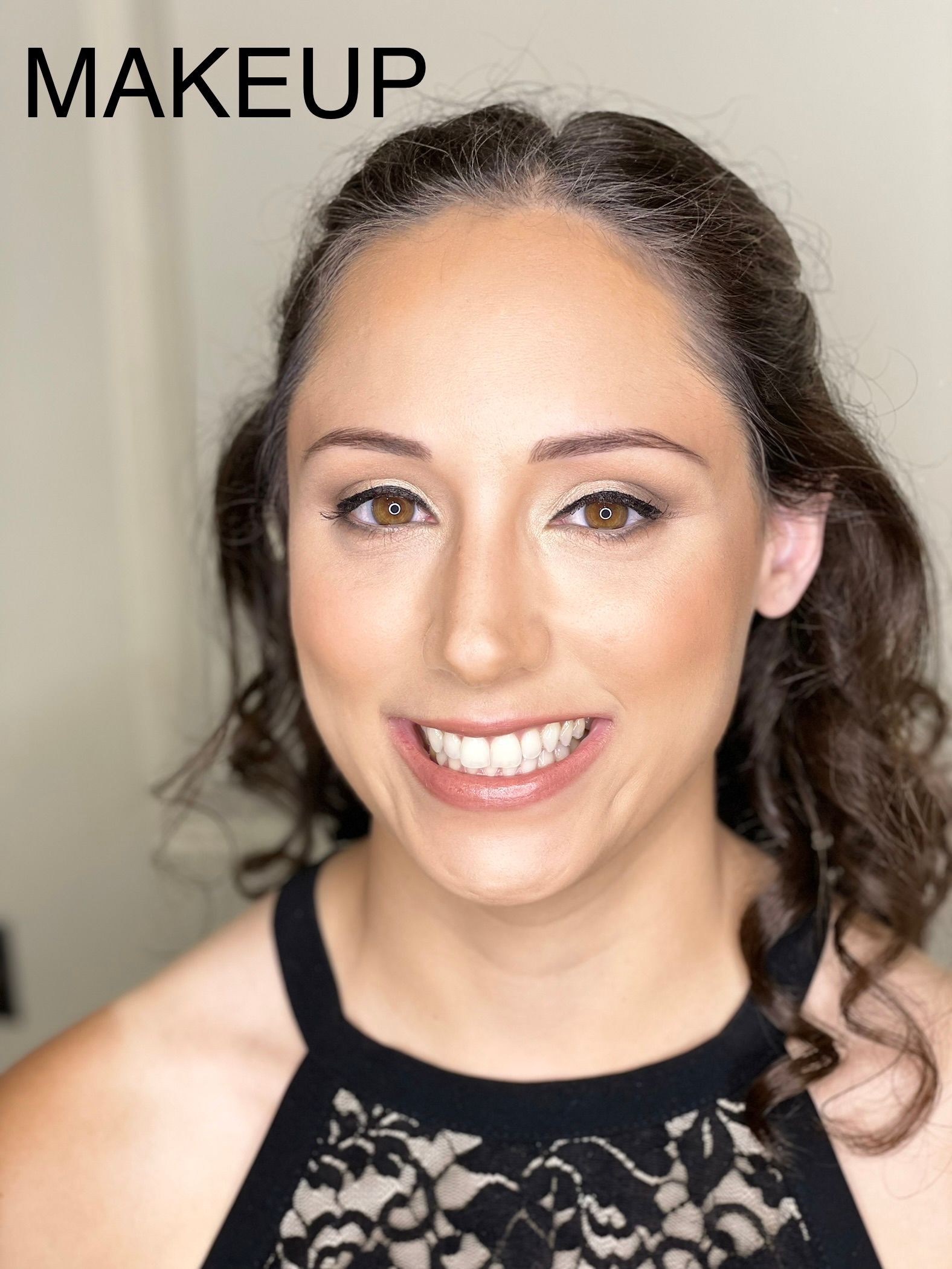 A woman with makeup on her face is smiling and wearing a black top.