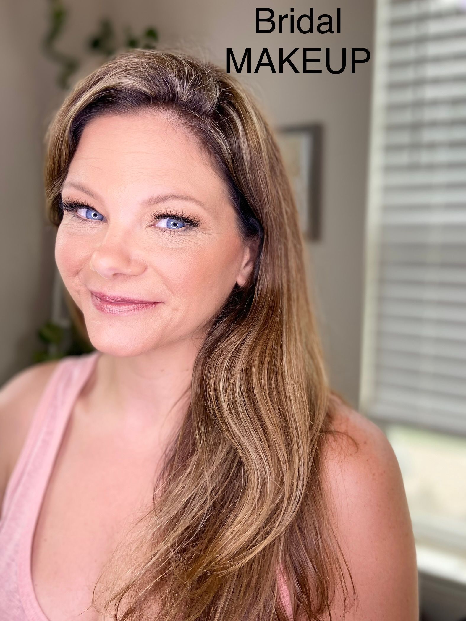 A woman with long hair and blue eyes is wearing bridal makeup.