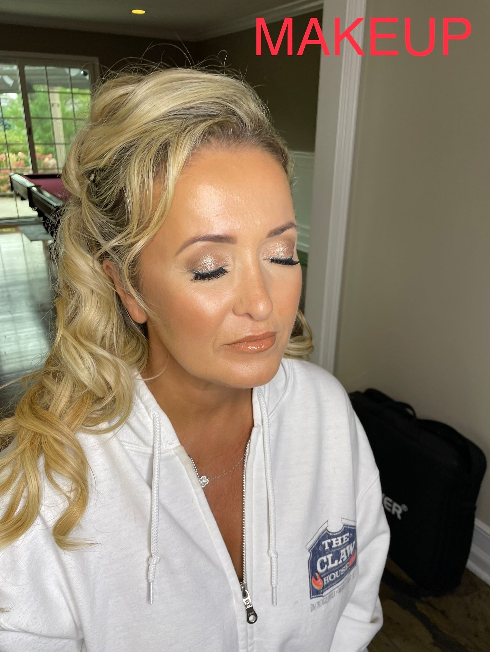 A woman in a white hoodie is getting her makeup done.