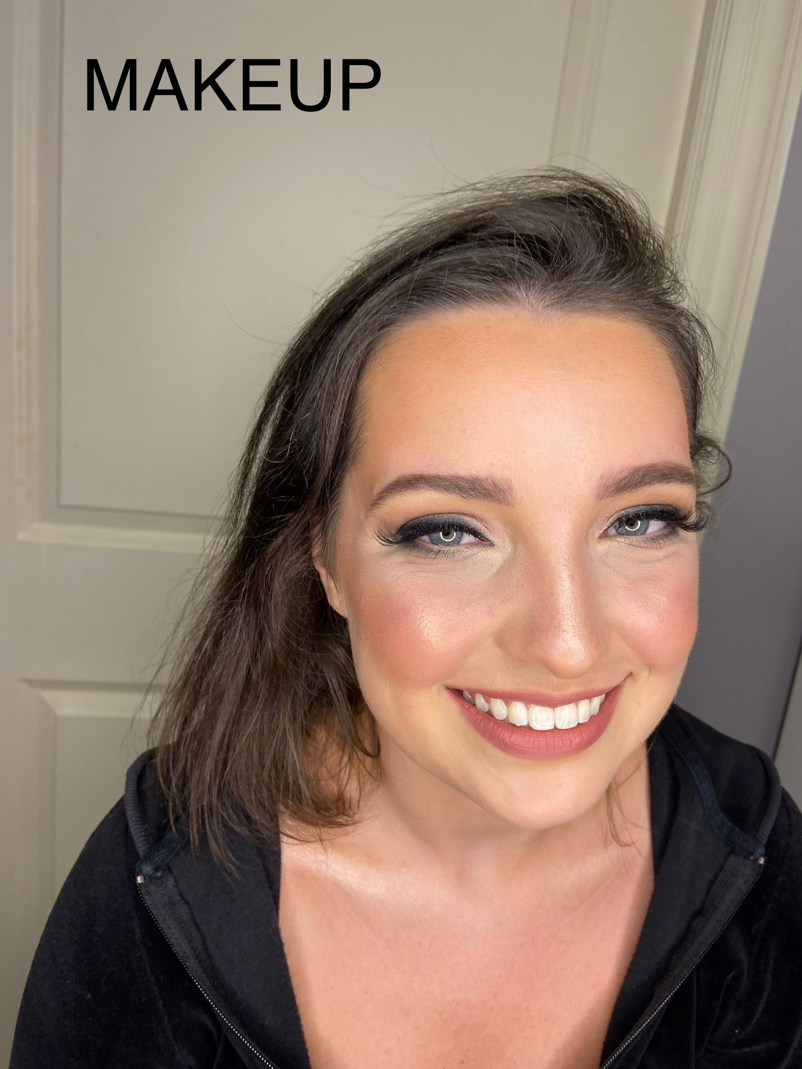 A woman with makeup on her face is smiling in front of a door.