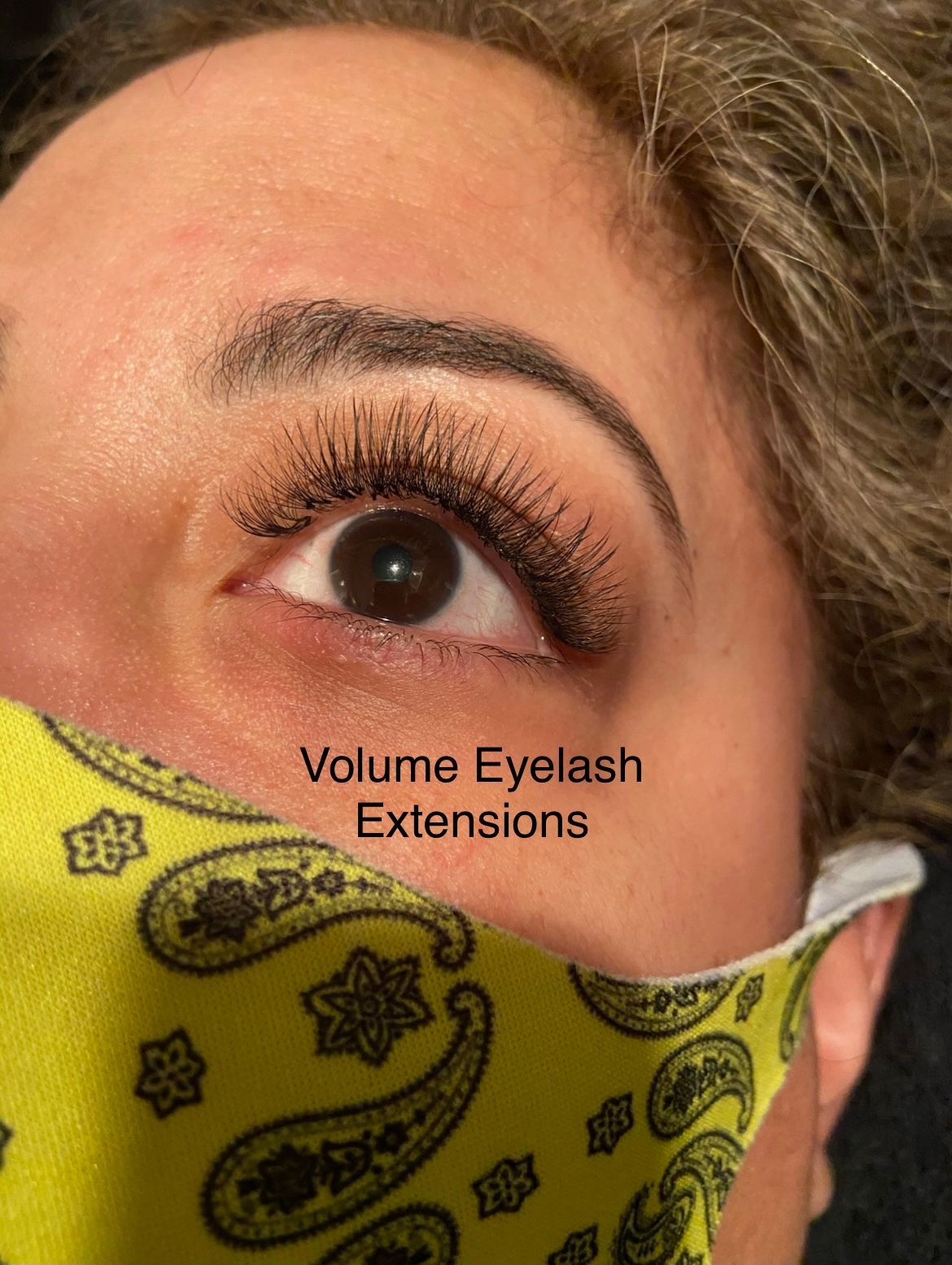 A woman wearing a yellow bandana has volume eyelash extensions on her eyelashes.
