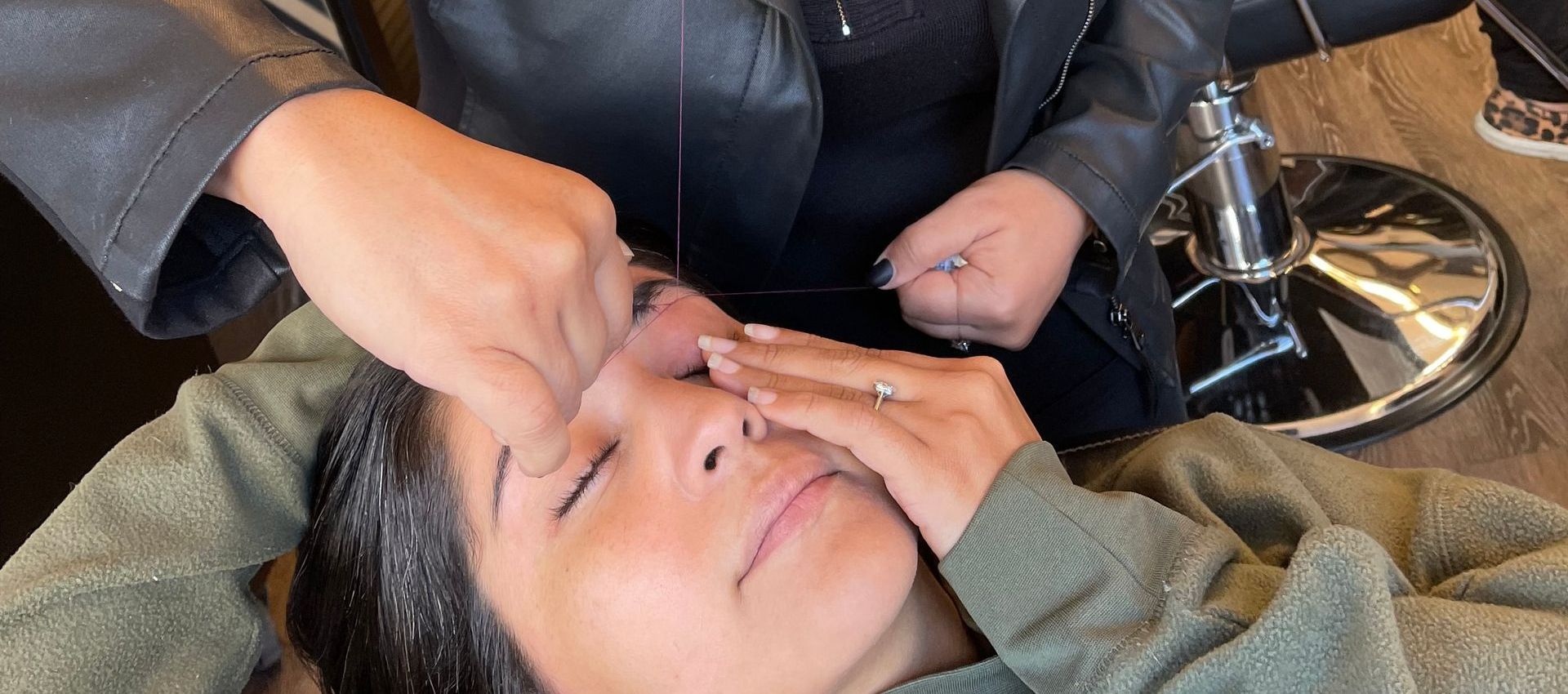A woman is getting her eyebrows threaded in a salon.