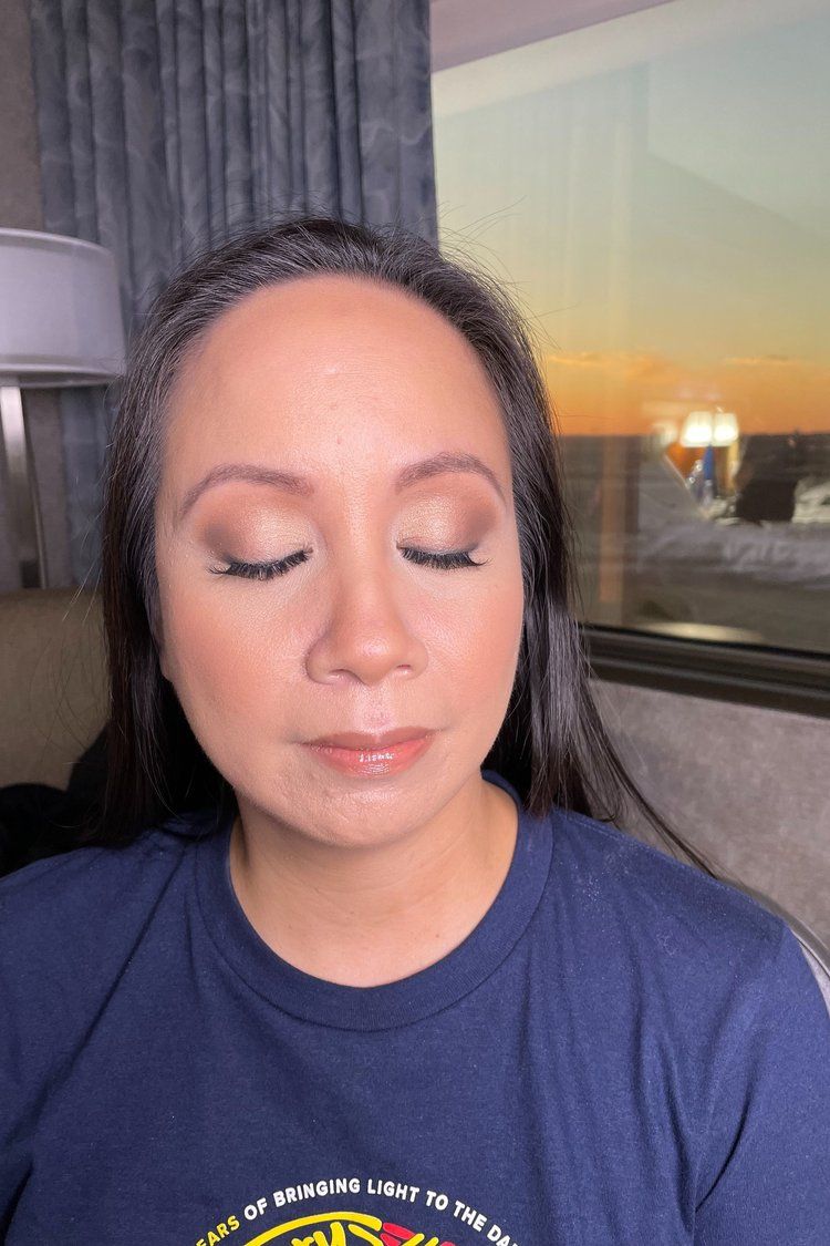 A woman wearing a blue shirt is sitting in front of a window with her eyes closed.