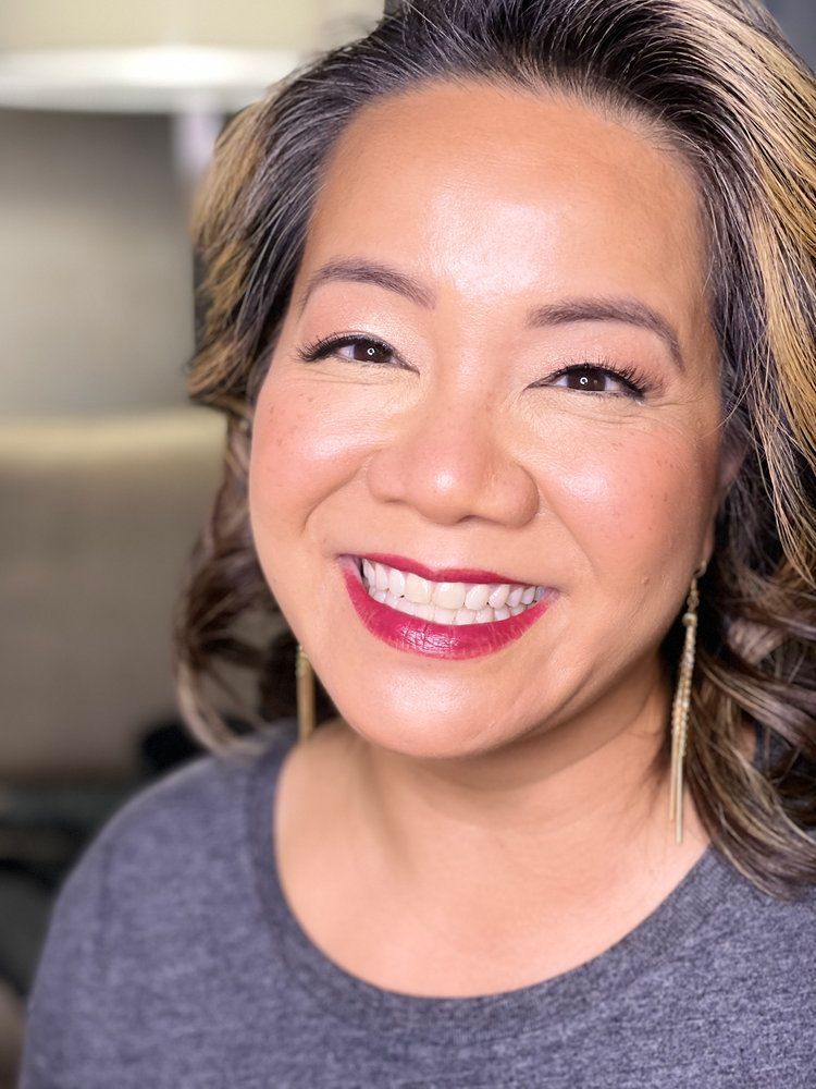 A woman wearing red lipstick and earrings is smiling for the camera.