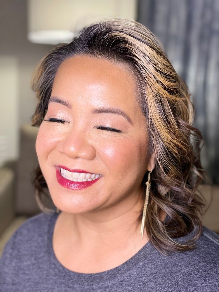 A woman is smiling with her eyes closed and wearing red lipstick.