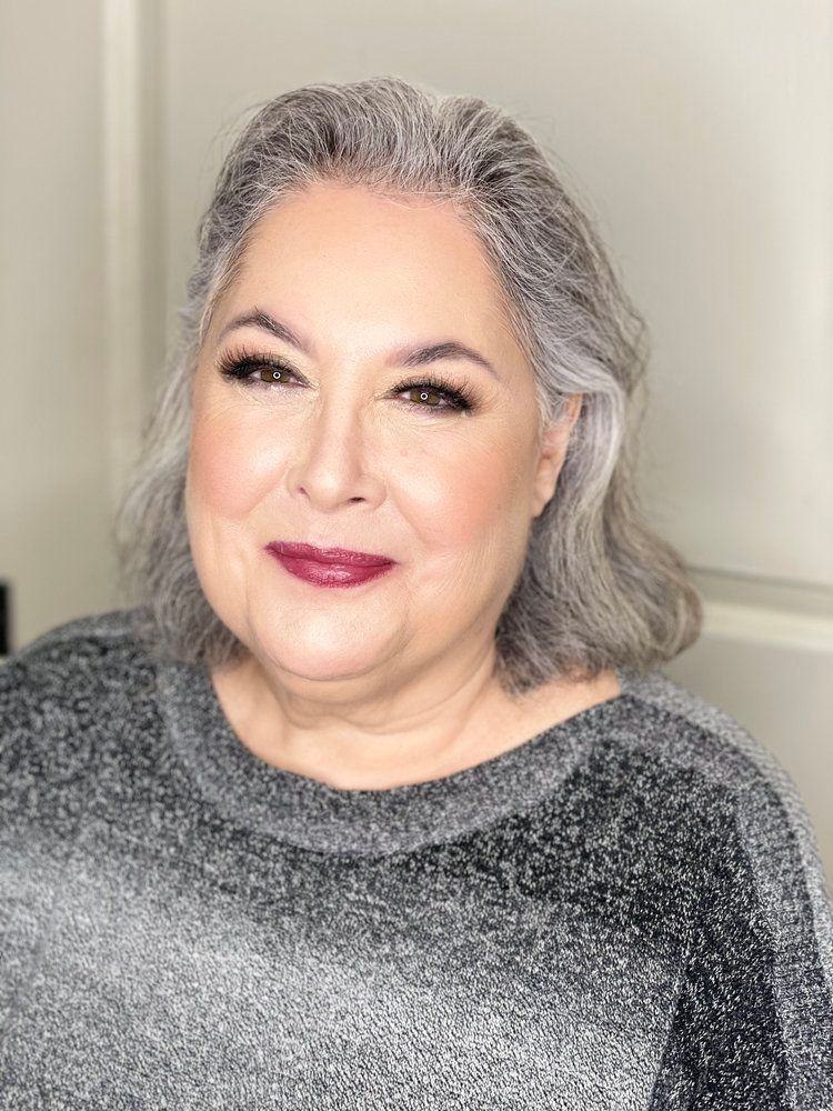 A woman with gray hair is wearing a gray sweater and red lipstick.