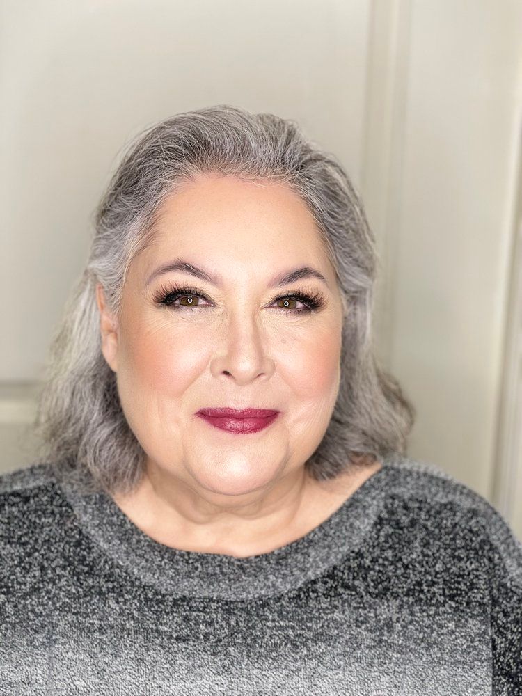A woman with gray hair is wearing a gray sweater and red lipstick.