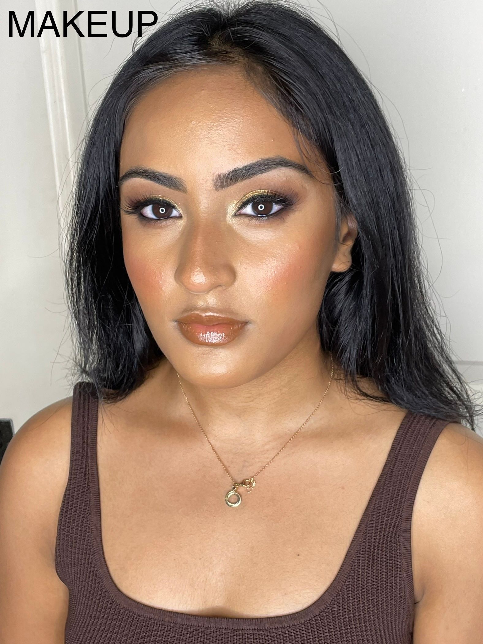 A woman is wearing a brown tank top and a necklace.