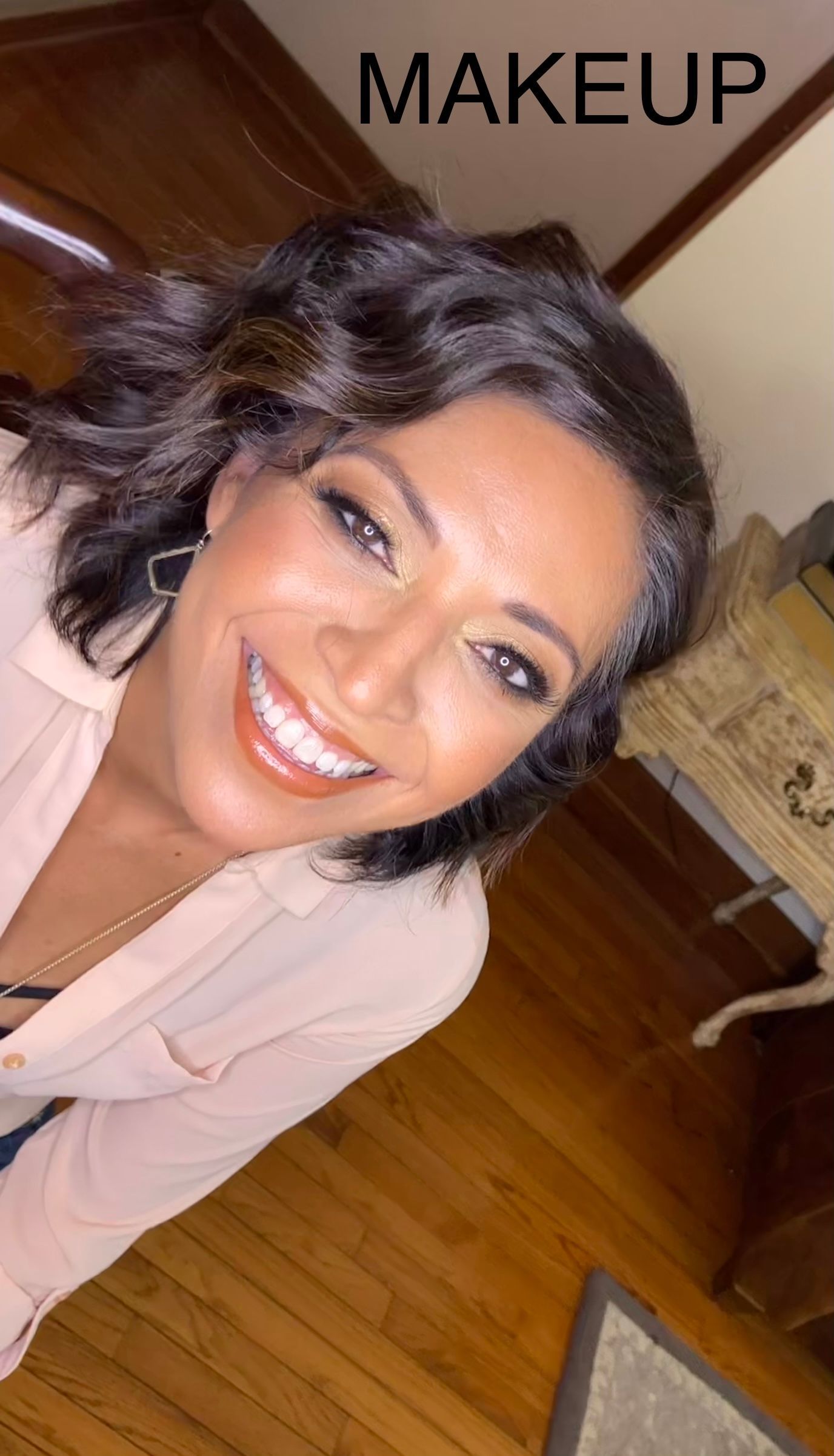 A woman is smiling and wearing makeup while sitting on the floor.