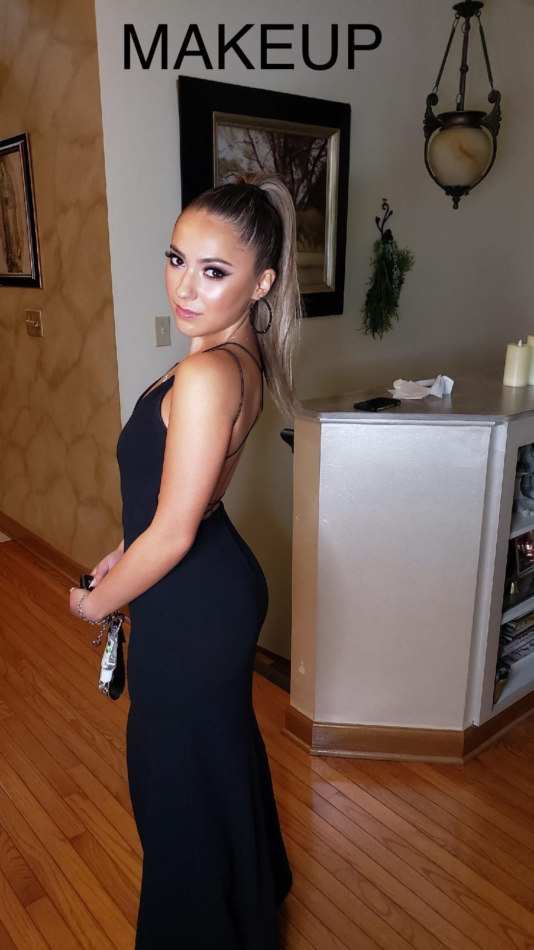 A woman in a black dress is standing in front of a sign that says makeup.