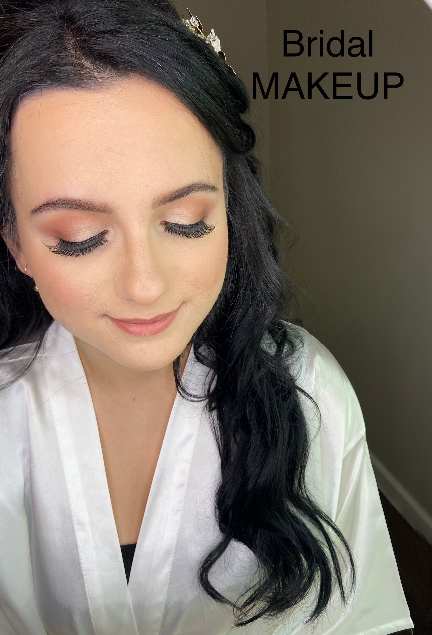 A woman is wearing a white robe and getting her makeup done.