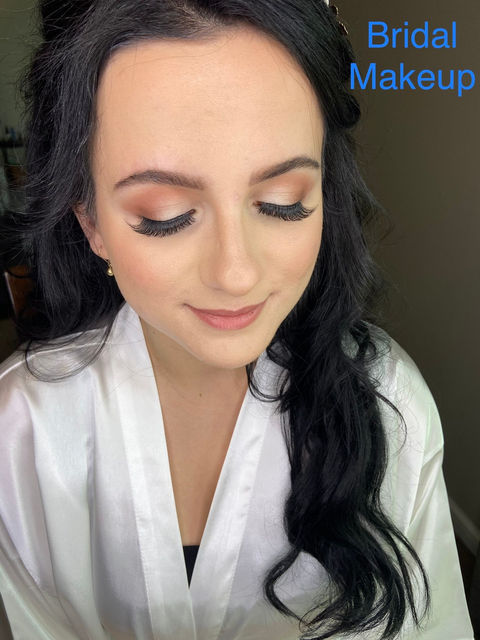 A woman is wearing a white robe and getting her makeup done.