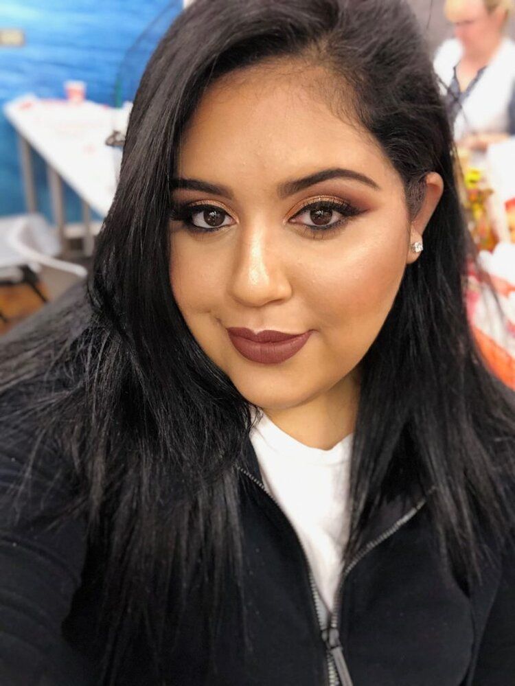 A woman wearing a black jacket and a white shirt is taking a selfie.