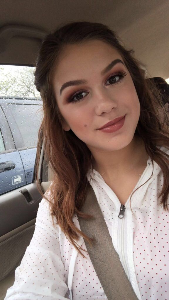 A young woman is taking a selfie in the back seat of a car.
