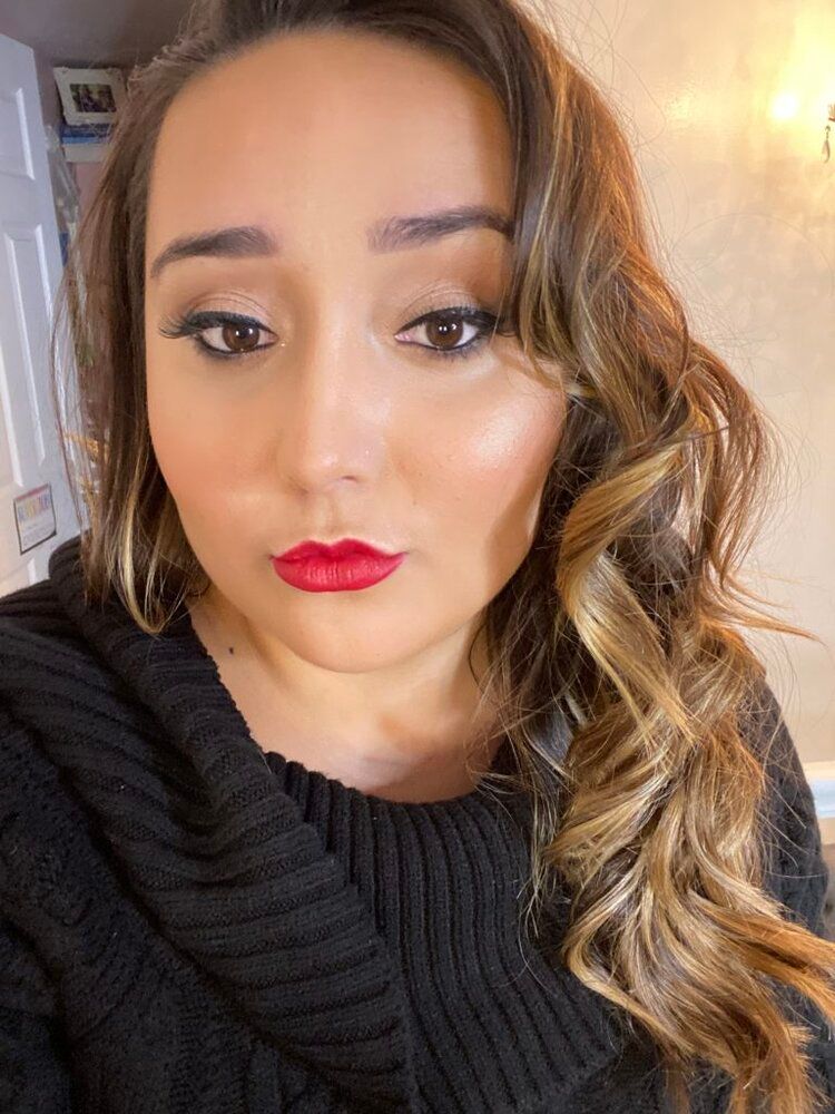 A woman wearing a black sweater and red lipstick is taking a selfie.