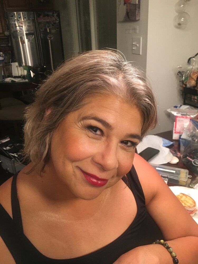 A woman in a black tank top is smiling in a kitchen.
