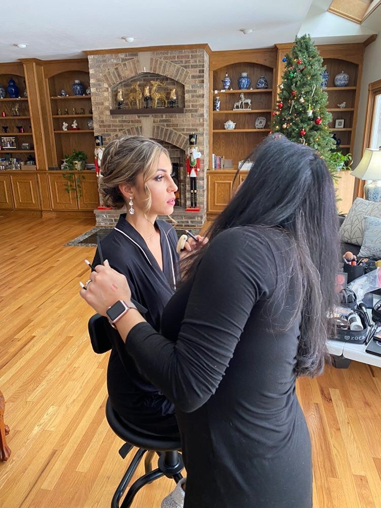 A woman is getting her makeup done by a makeup artist in a living room.