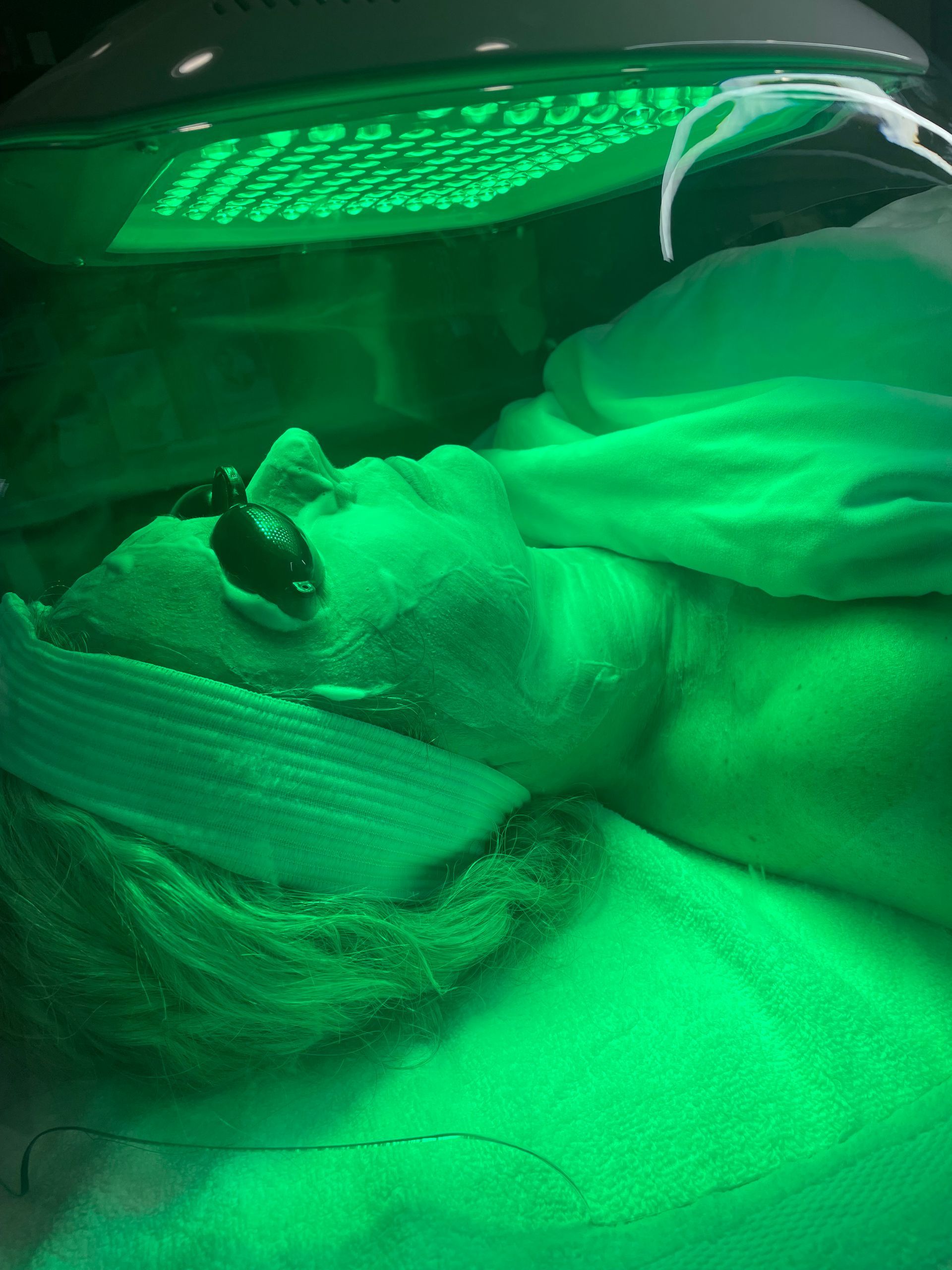 A woman is getting a green light treatment on her face.