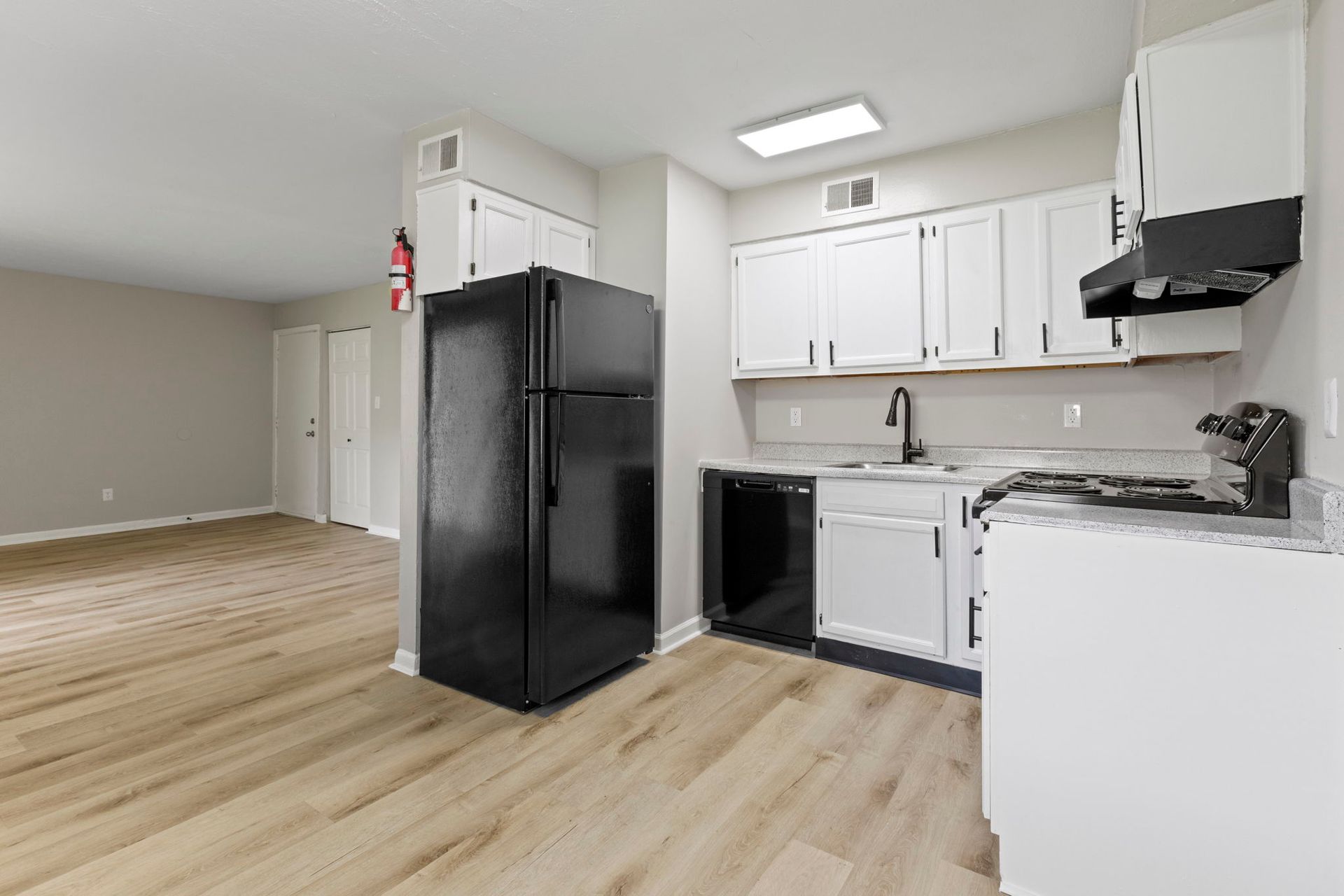 Kitchen with black appliances, white cabinets, light wood floor, and gray walls.