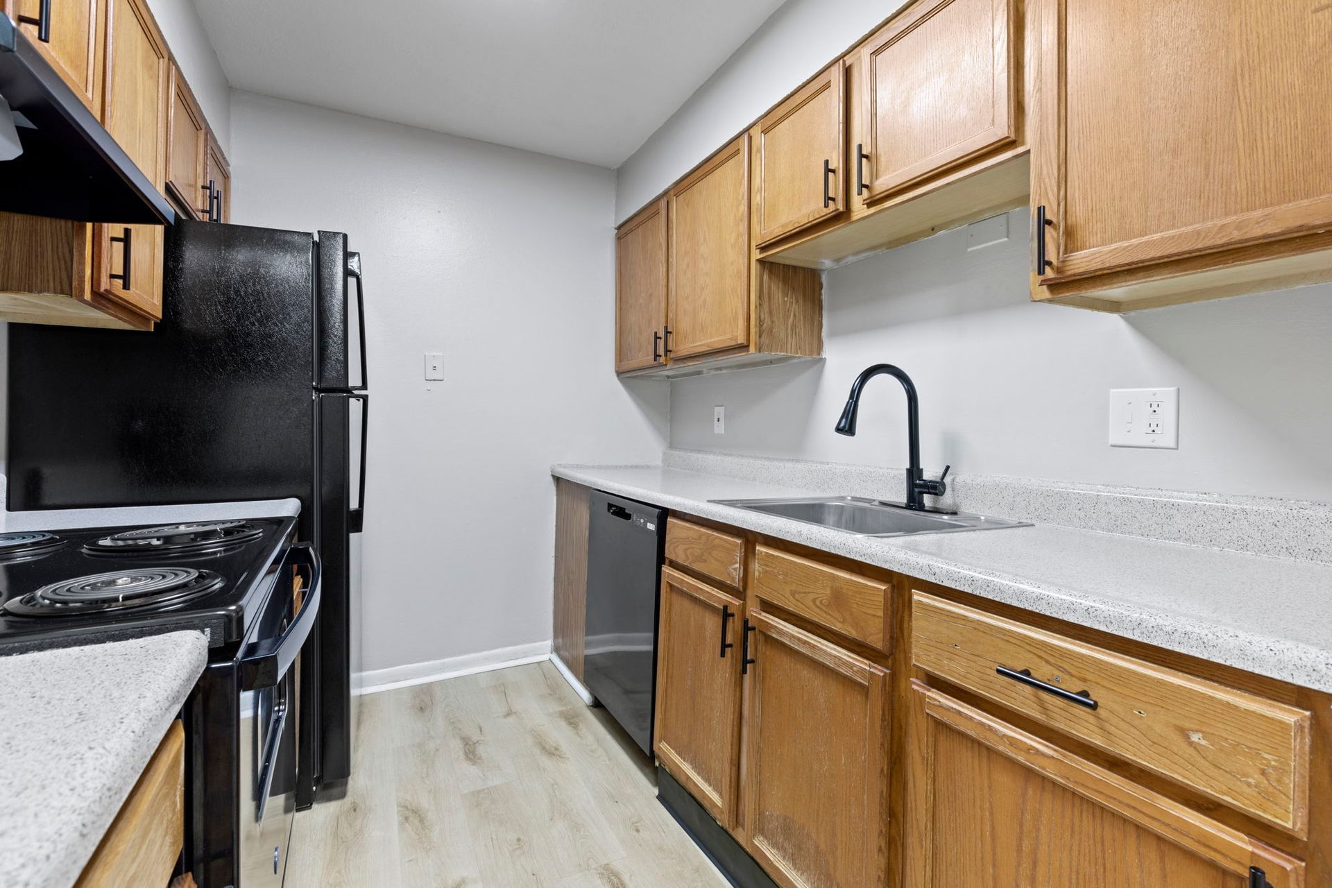 A kitchen with wooden cabinets, black appliances, a stainless steel sink, and a white countertop.